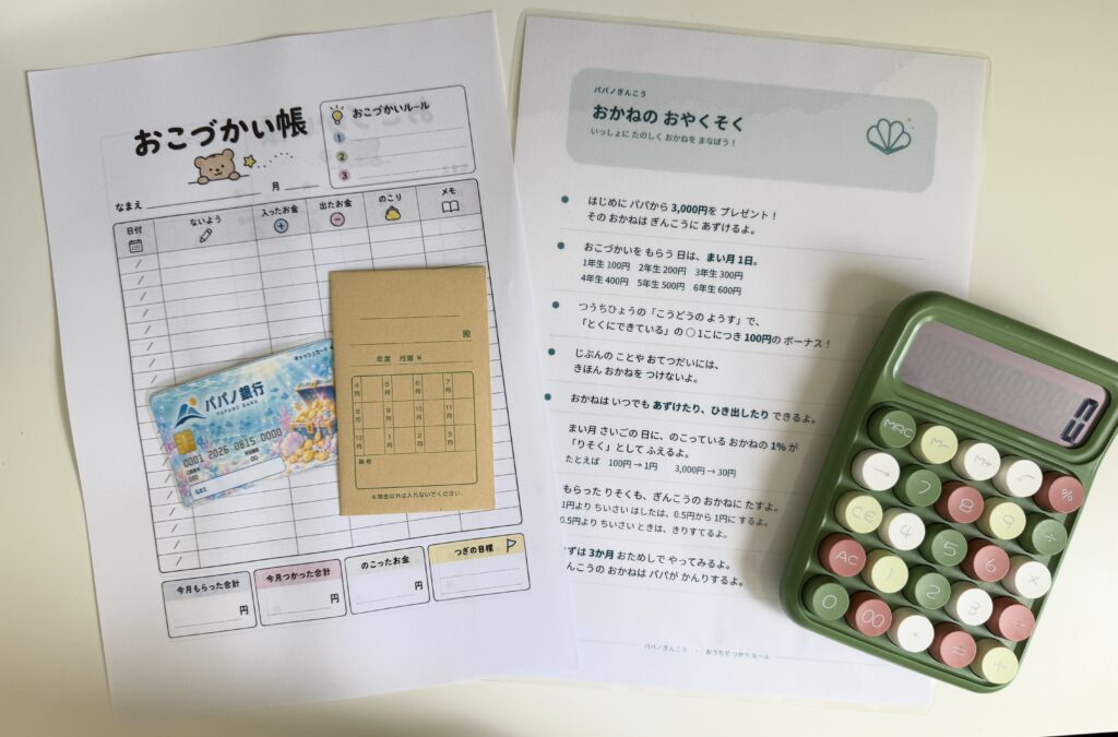 パパノ銀行のキャッシュカード、通帳、お小遣い帳、ルール表、緑色の電卓を並べた写真